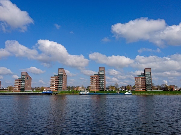 Foto van woningen aan het water met een blauwe lucht met wolken